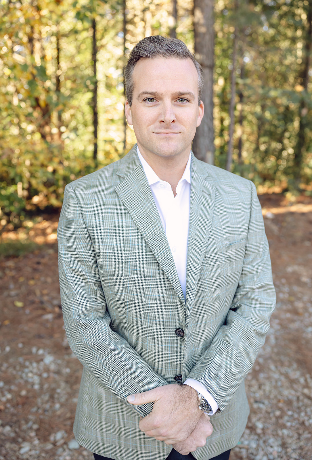 A man in a suit standing outside near some trees.
