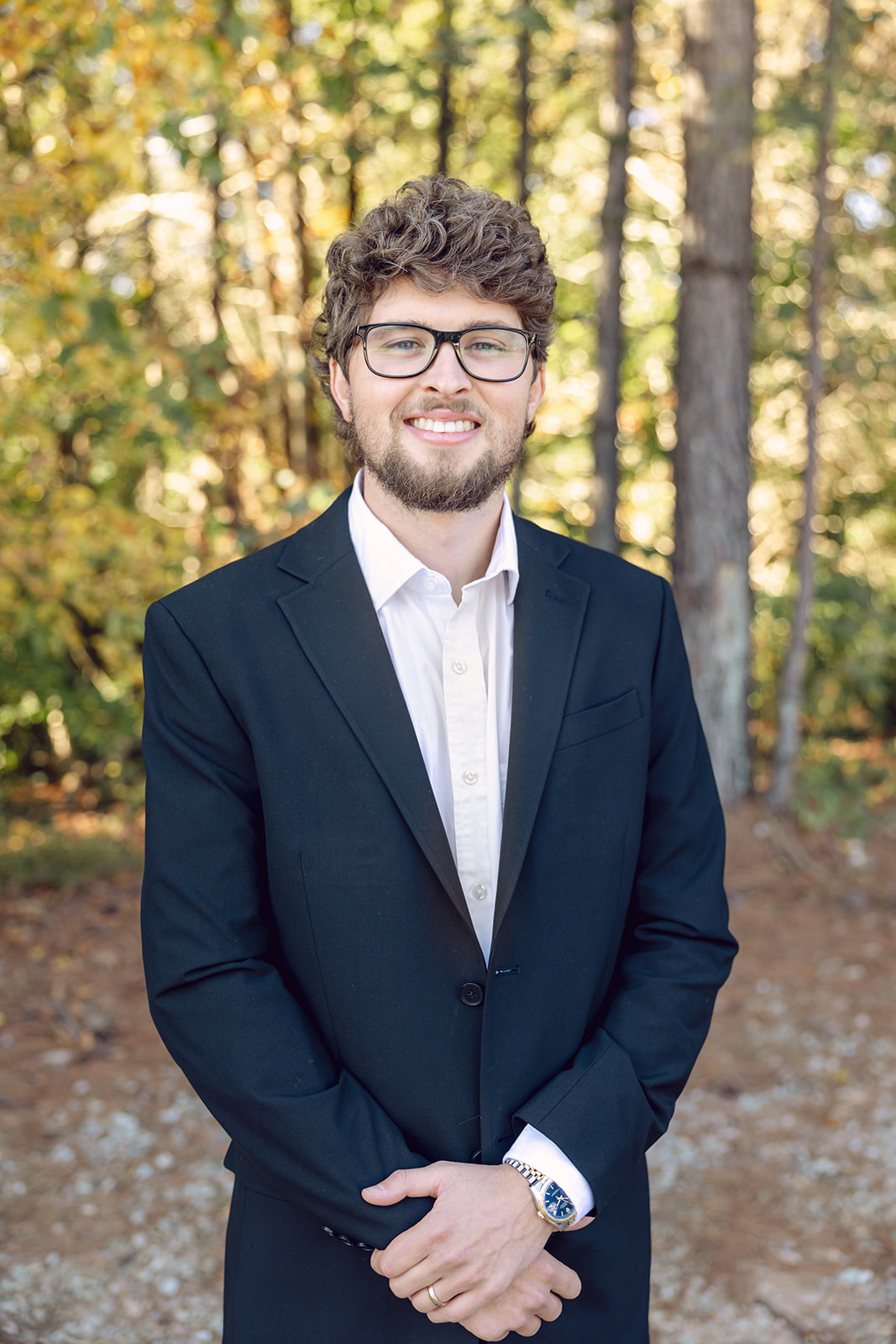 A man in a suit and glasses standing outside.