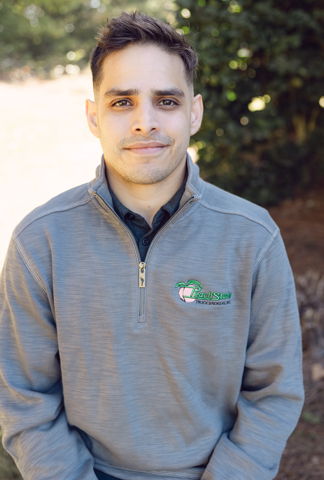 A man in grey sweater standing next to tree.
