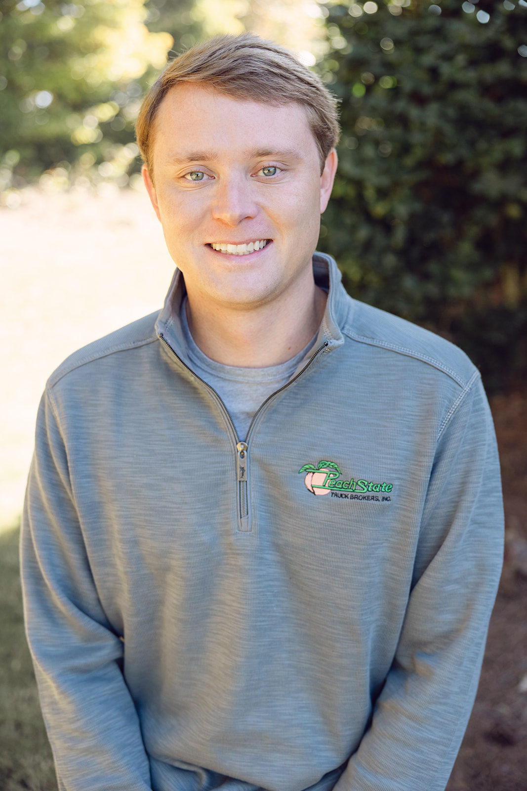 A man in grey shirt standing next to bushes.