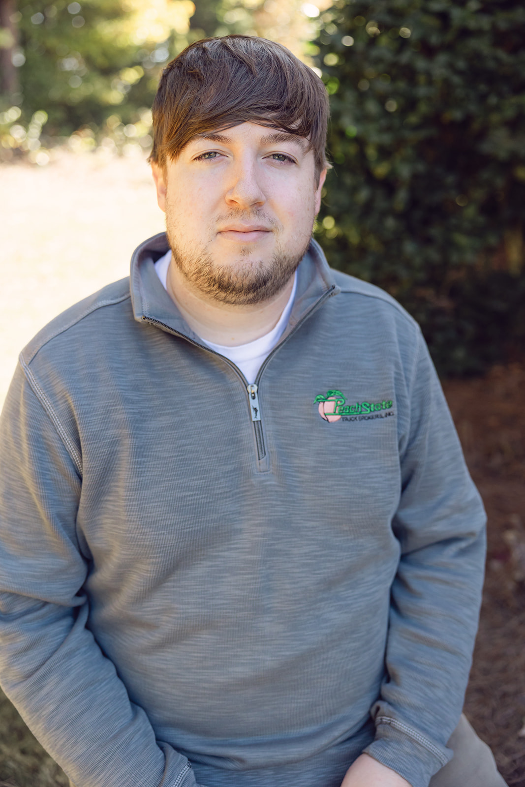 A man in grey sweater standing next to trees.
