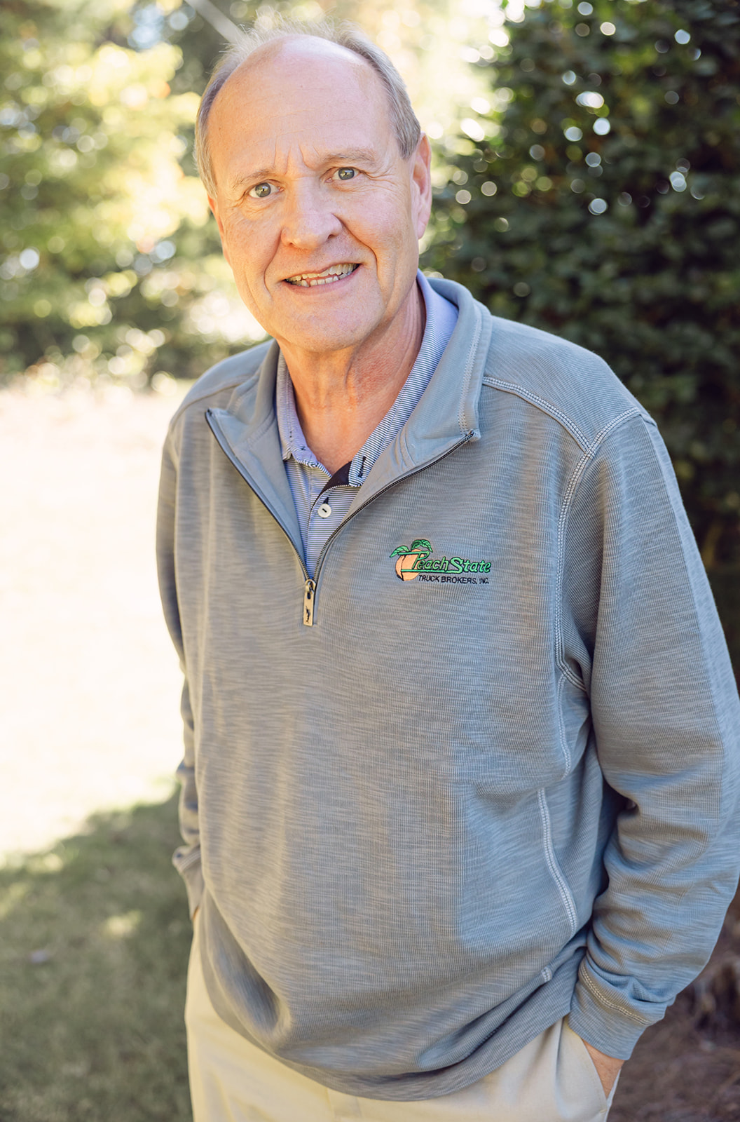 A man in grey jacket standing next to tree.